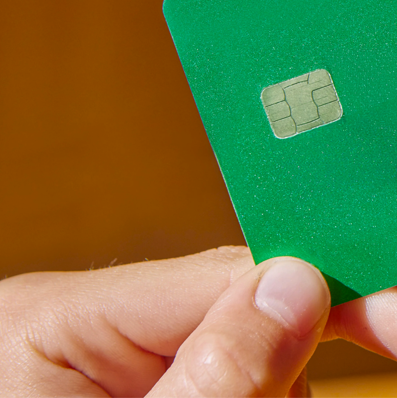 A hand holding a green card with a visible metallic chip.