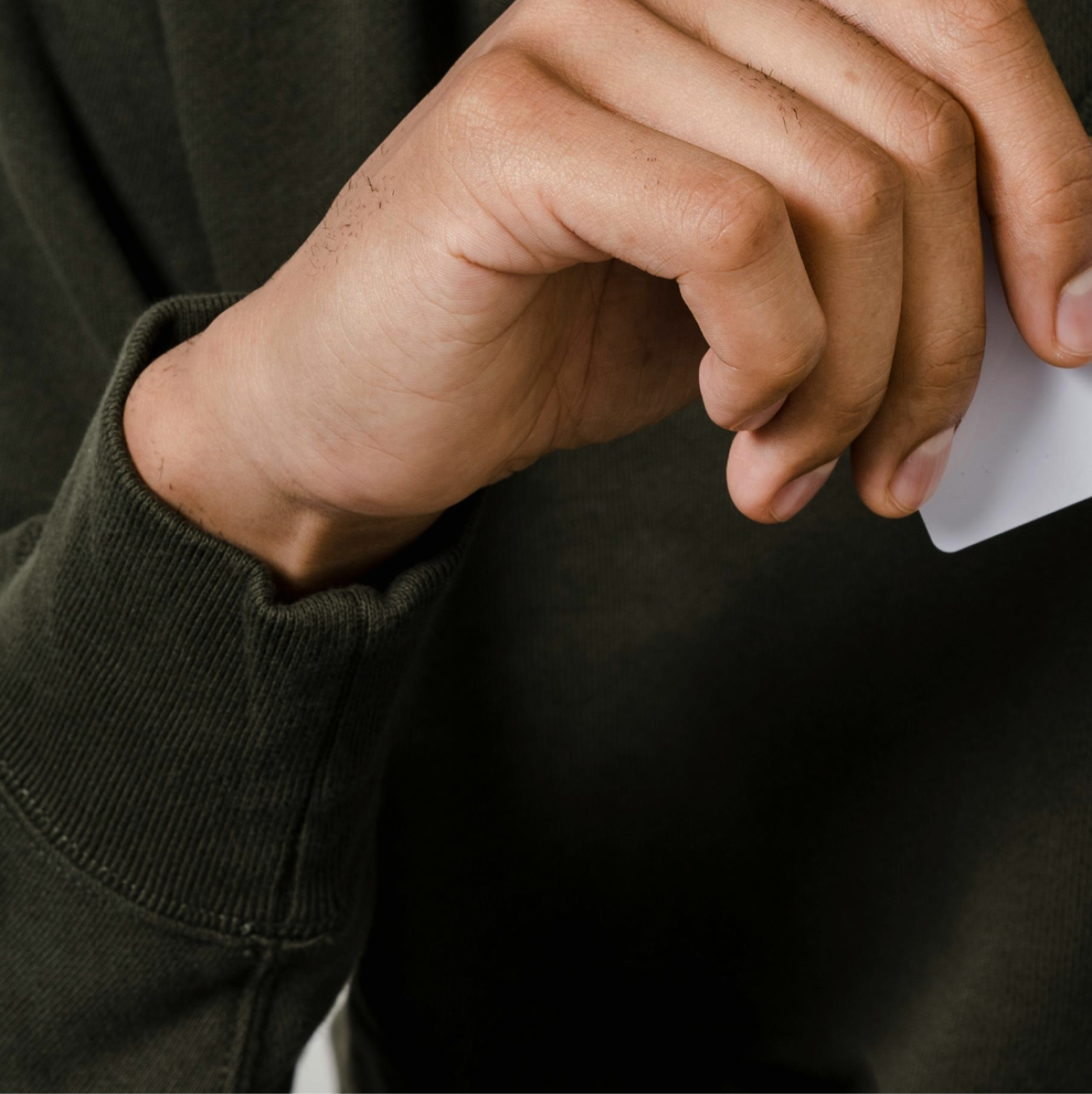 Hand in dark green sleeve holding a white card.