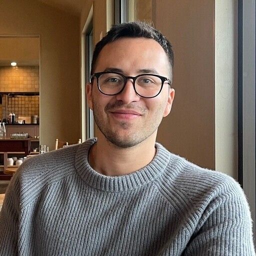 A man with glasses and a grey sweater smiles at the camera.