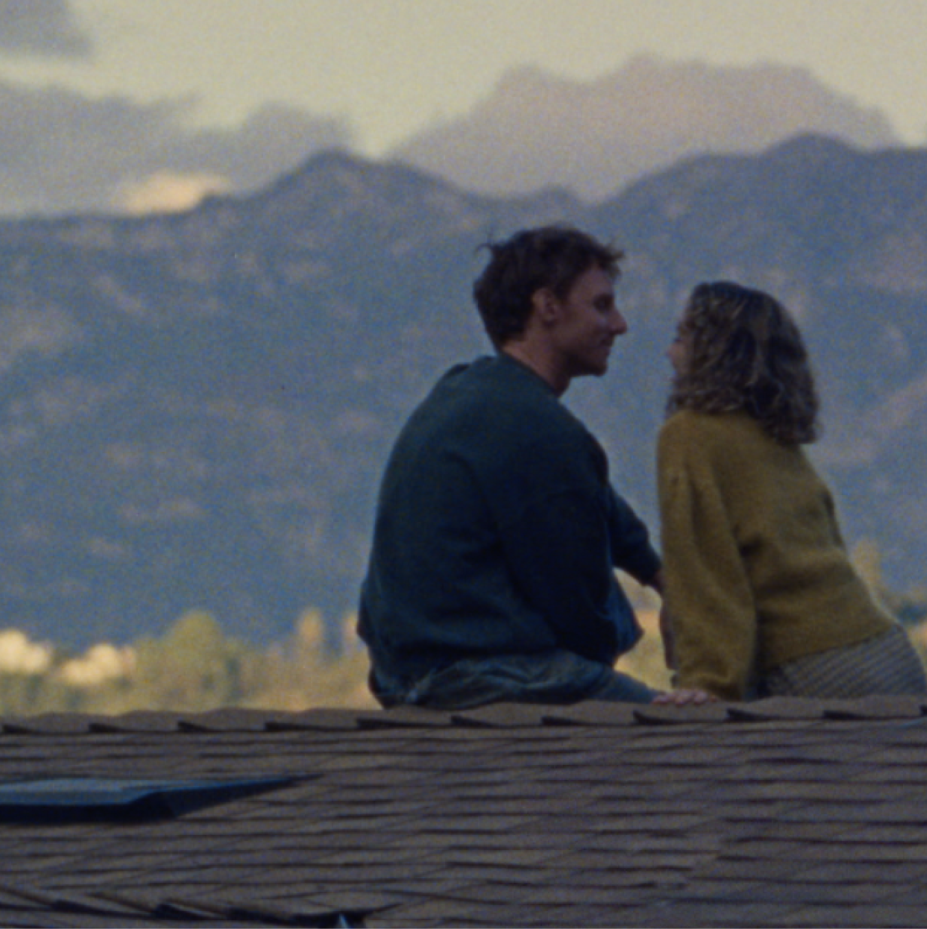 Couple sitting on a rooftop, gazing at each other with mountains in the distance.