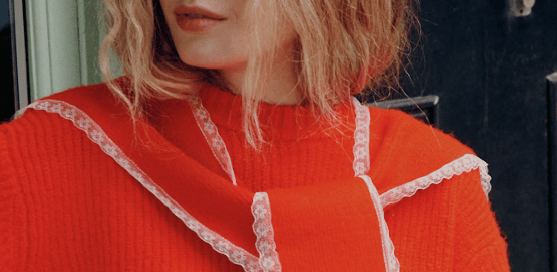 Close-up of a woman in an orange ribbed sweater with a matching scarf trimmed in white lace.