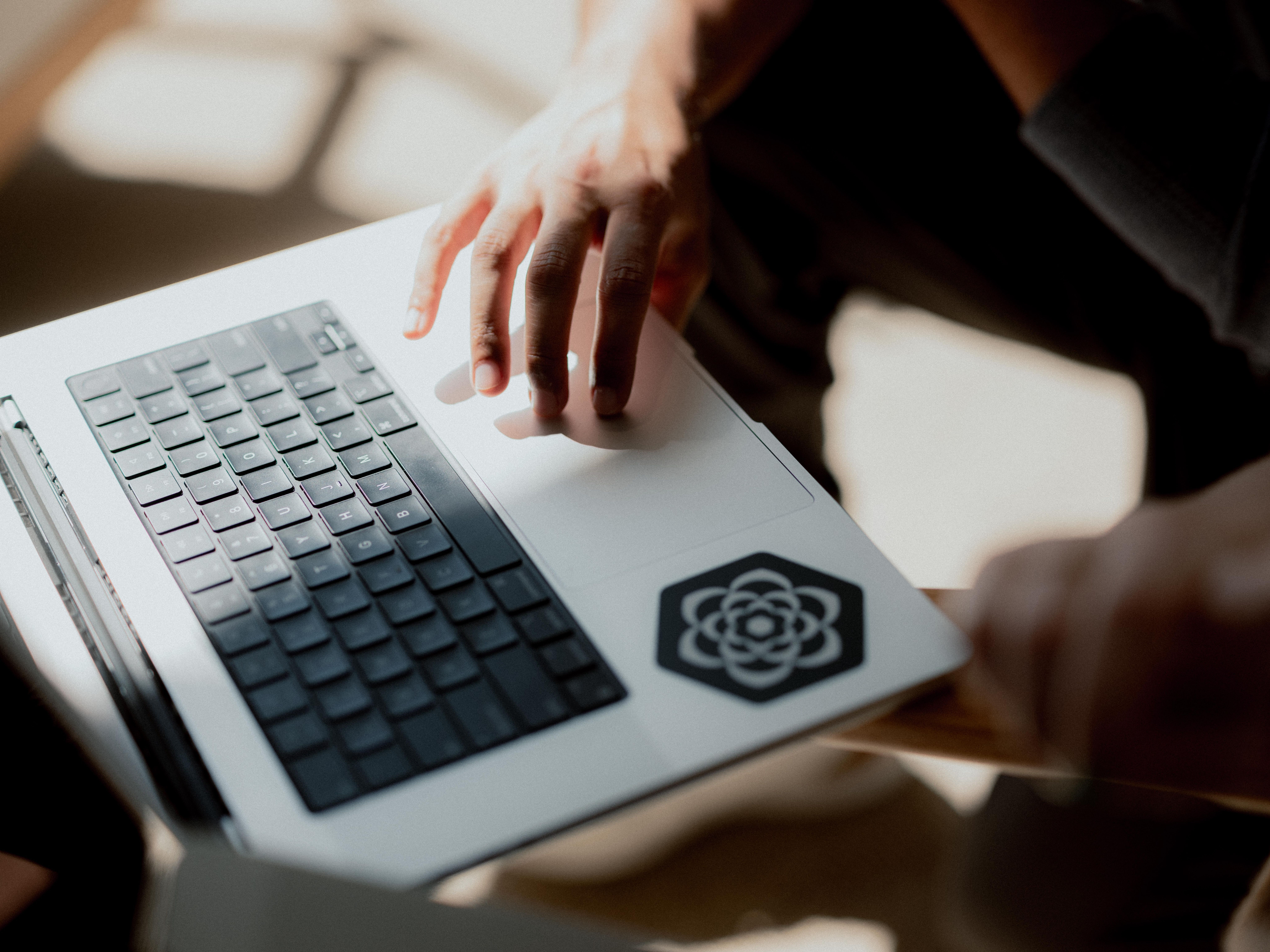 Top-down close-up of a laptop. You can see someone's hand using the Laptop's trackpad